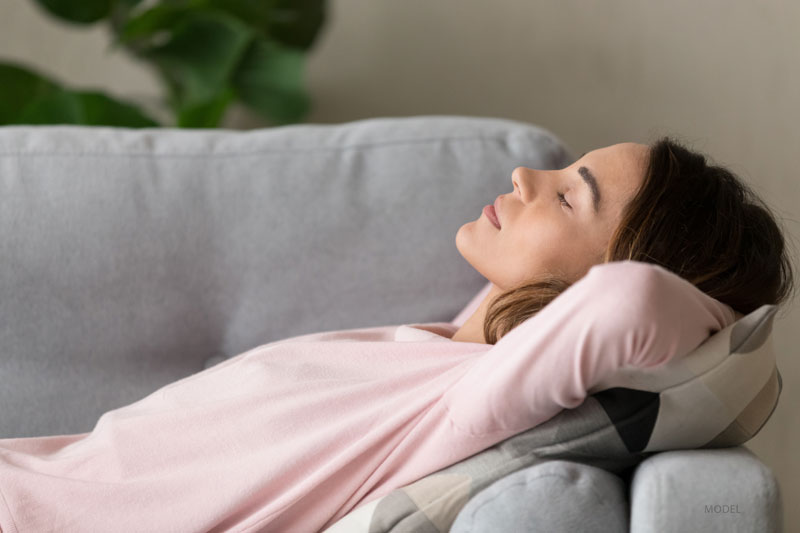 Woman relaxing on a couch with her arms under her head.