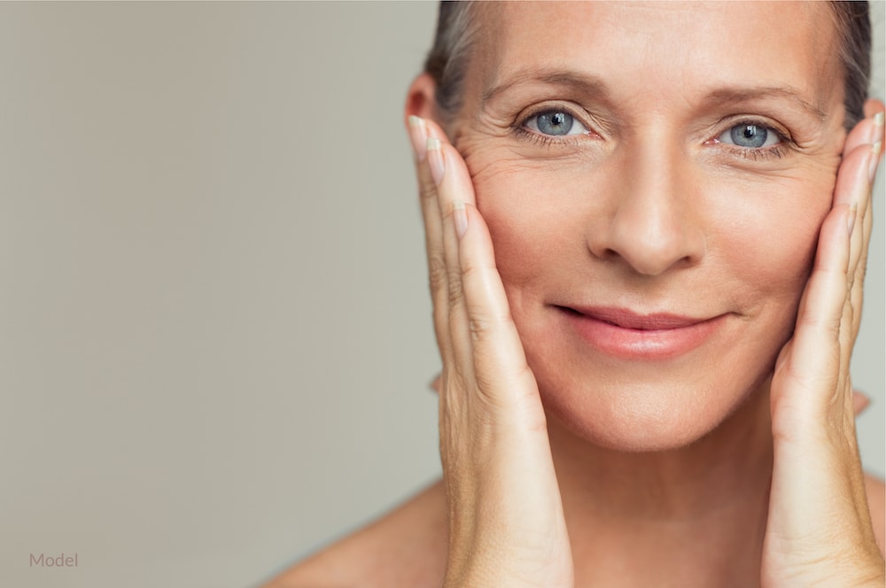 Woman fulling the skin back on her face to see the potential results of a facelift.