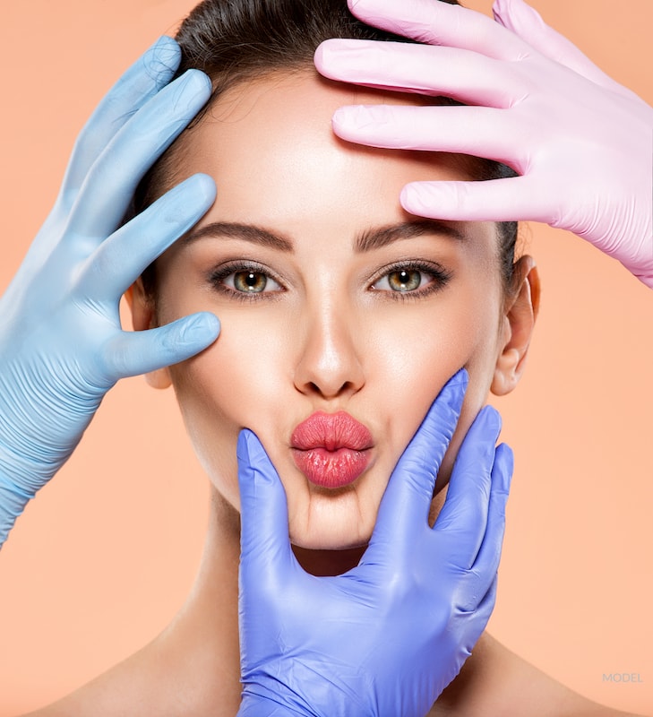 Woman puckering her lips with her face surrounded by doctor's hands.