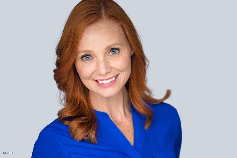 Close up image of a smiling, middle-aged woman wearing blue. This shows potential results with facial rejuvenation procedures.