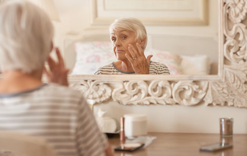 Elderly woman studying her reflection in the mirror while touching the side of her face