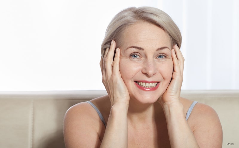 Beautiful middle-aged woman, smiling while placing her hands on either side of her face.